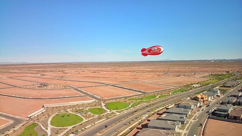 Red NEW HOMES advertising blimp flying high above a new home community, visible for miles