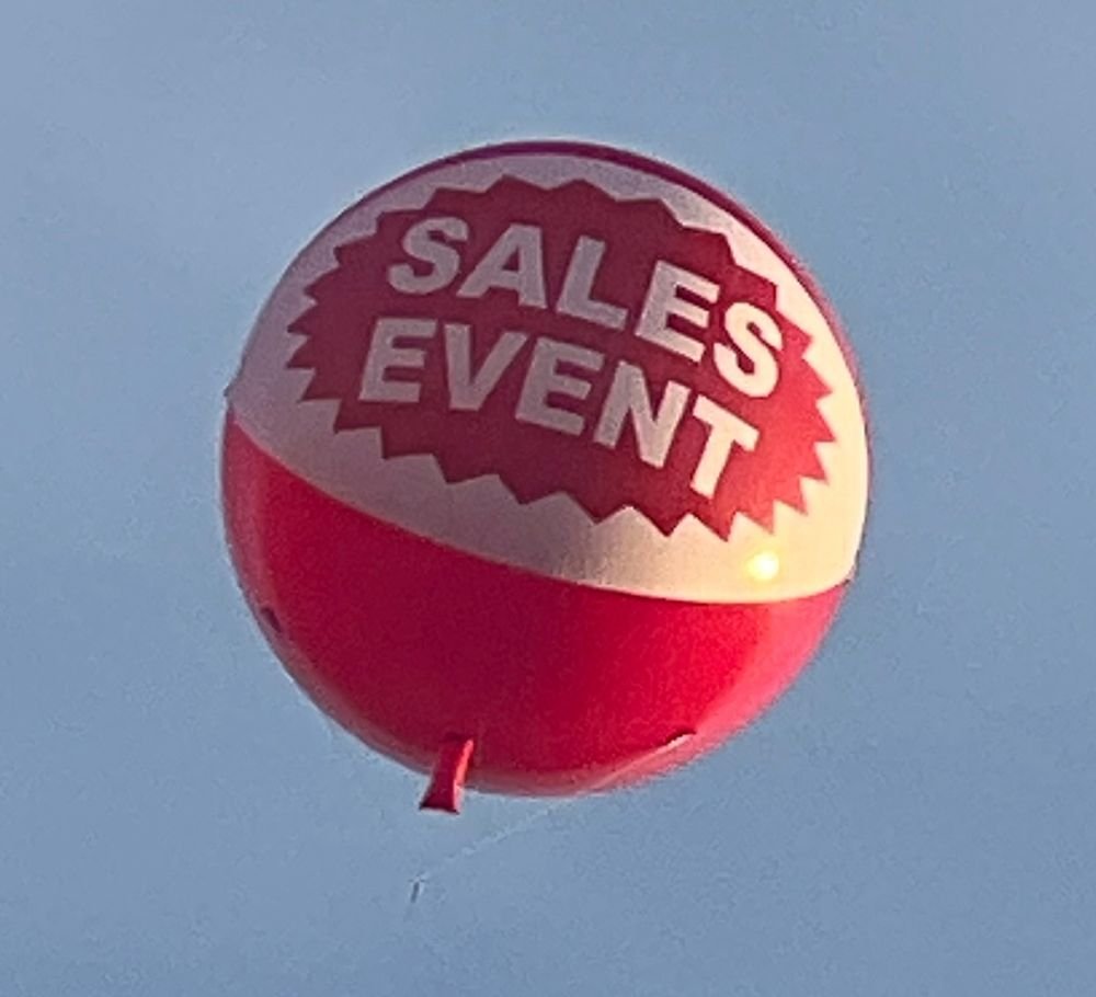 Giant helium sales event advertising balloon flying above a dealership